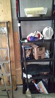 Black shelving unit in garage holding various items, including booster cables, heater, boxes, and car mats
