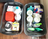Two black laundry baskets filled with assorted laundry and cleaning supplies viewed from above showing bottle tops, containers, and packaging details.