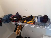 Clothing items including belts, folded clothing, hats, socks in a bag, and hangers on a wire shelf and hanging below