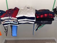 Folded men's shirts and sweatshirts on a rack with hangers beneath