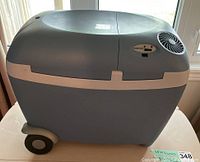 Full front side view showing blue plastic portable cooler/heater with wheels and handle on left side.