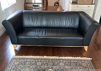 Front view of three-seat black leather sofa showing seat cushions, backrest, armrests, and wood legs