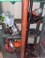 Three-level metal shelving unit with various tools and cords including Black & Decker circular saw, drill, extension cords, and work light