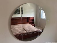 Front view of the round folding mirror mounted on the wall, showing reflection of the room.