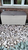 Front view of the plastic storage chest positioned outdoors on a bed of rocks against a brick wall.