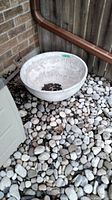 Full view of the round outdoor ceramic planter placed on river rocks with a weathered white finish.