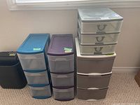 Four plastic drawer storage units of different sizes and colors placed on the floor near a window.
