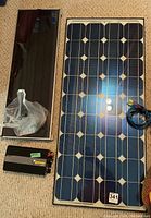 Photo showing Xantrex Inverter 100 power supply, smaller reflective solar panel, and large solar panel with cable
