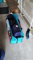 Several packed tent bags including a large blue and red duffel bag and a dark blue bag with a 505 tag, organized on a concrete floor near a broom and shelving unit.