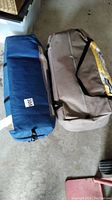Two large duffel bags on a concrete floor containing the tent and accessories.