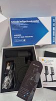 Open box showing two black handheld microphones in foam packaging, along with USB cables and mounting accessories, and a user guide booklet.