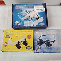 Three boxed watch repair magnifiers: white digital microscope loupe, yellow LED magnifier, and black upgraded watch repair magnifier