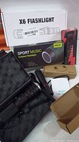Photo showing boxed X6 Fiashlight, Sport Music Outdoor Flashlight box, a smaller boxed flashlight, and tactical flashlight in foam case