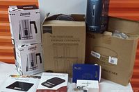 Wide shot showing all items: two boxed Zeppoli milk frothers, a box of air-tight food storage containers, two electronic scales, a boxed cake pan, and other items.