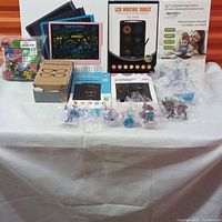 Overview photo showing two boxed LCD writing tablets, 3D glasses box, several action figures in plastic packaging, and some Rubik's cubes.