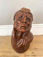 Front view of expressive wood composite carving face, showing detailed closed eyes, brow, nose, mouth, and hair flowing back.