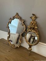 Pair of gold gilt wood mirrors on wooden surface, showing overall shape and design