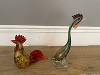 Front view of two art glass rooster sculptures, showing color, form, and detail.