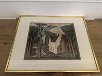 Framed print showing a landscape with a house, trees, and sky in muted colors, taken from above on wooden floor.