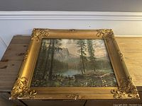Full view of ornate gold frame and landscape print showing forest, mountains, lake, and hikers.