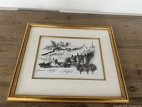 Framed black and white sketch on a wooden surface showing artwork and signature clearly.