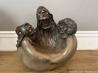 Front view showing all three carved faces and flowing hair detail in a connected embrace sculpture.