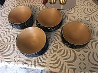 Four Japanese bowls shown with interiors facing up, displaying natural wood tone with smooth finish and dark blue exteriors adorned with white floral and geometric designs.