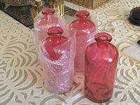 Four pink glass bottles grouped with some bubble wrap. Bottles have a vivid raspberry pink color and wide neck openings.
