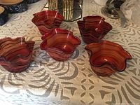 Five hand blown glass bowls arranged on a patterned cloth surface showing organic wavy rims and swirl patterns in red and black hues.