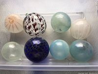 Top-down image of eight different colored handblown glass ornaments arranged in two rows, showing multiple styles and colors.
