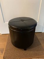 Side view of round black faux leather ottoman stool showing cylindrical shape and stitched panel design.