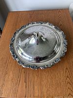 Top view of silver plated covered dish with ornate floral and scroll edge and domed lid with knob