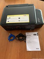 Epson Expression ET-2550 EcoTank printer viewed from top-down angle, showing included USB and power cables plus quick guide manual on table.