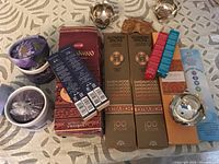 Top-down image of new incense packages and three used metal incense holders on patterned cloth.