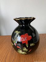 Front view showing black ceramic vase with red flowers and gold trim on wavy rim.