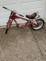 Side view of the full bicycle showing red frame with flame graphics, front handlebar, large rear tire, and kickstand.