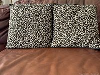 Two leopard print cushions on a brown leather couch showing front sides with pattern