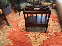 Full view of vintage mahogany magazine rack on decorative rug showing the compartments and lower shelf.