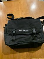 Front view of the black canvas computer bag with flap and two buckles displaying the 'Micron' brand name.