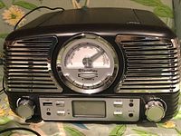 Front view of TechPlay retro style music player showing chrome speaker grills, central circular dial, volume and tuning knobs, USB port and LCD display