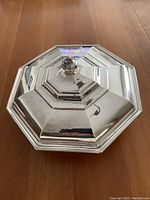 Octagonal silver plated covered casserole dish with faceted knob lid resting on wooden surface.