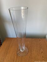 Tall clear vee shaped glass vase standing on wooden table against plain background