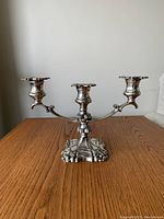 Front view of the Victorian coronet plate silver candelabra showing three candle holders with floral and scrollwork ornate design and sturdy decorative base.