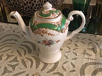 Side view of a vintage Tuscan bone china teapot showing floral decoration, green and gold pattern, with curved handle and spout.