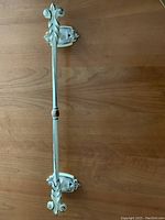 Full view of the vintage metal towel rack showing the cream painted body with gold-tone accents and mounting brackets on a wood surface.