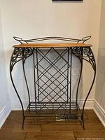 Front view of metal wine rack with decorative scrollwork, lattice bottle holder, and lower shelf on wood flooring.