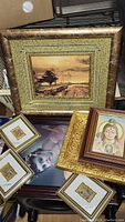 Photo of various framed art pieces including a rustic landscape painting and small framed artworks on top of a photographic portrait.