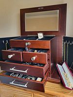 Open wooden jewelry box showing top compartment with mirror, multiple drawers and jewelry inside