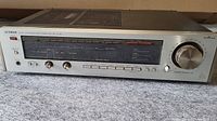 Front view of the Luxman R-406 stereo receiver showing the tuning dial, control knobs, and buttons, along with the power button and headphone jack.