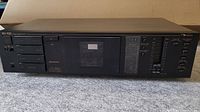 Front view of Nakamichi BX-100 cassette deck showing controls, cassette compartment, and digital level meters on a carpeted surface.